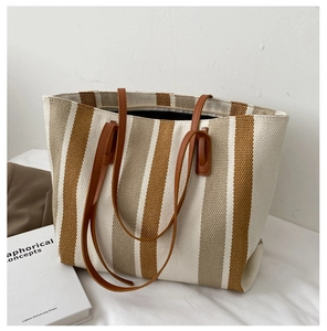 Detail of the large striped canvas tote bag featuring brown leather handles and spacious interior