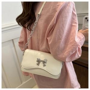 Detail view of a white butterfly bow crossbody bag featuring silver chain straps on a model