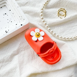 Close-up of bright orange clog shoe phone grip with sunflower and smiley face charm