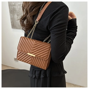 Detail view of caramel brown quilted crossbody bag with gold metal lock and chain strap