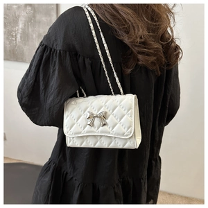 Close-up of white quilted chain bag with silver bow detail worn by model in black dress