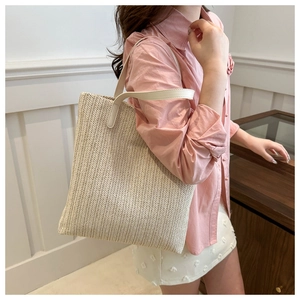 Close-up of beige woven straw tote bag with long leather shoulder straps on a model
