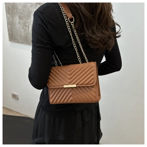 Close-up of brown quilted crossbody bag with V-shaped stitching and gold chain strap
