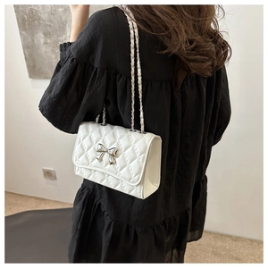 Rear view of model wearing white quilted crossbody bag with silver bow detail
