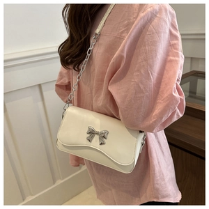 Detail of cream shoulder bag featuring silver butterfly buckle and chain strap on model