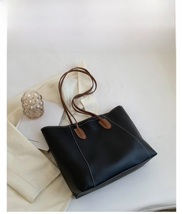 Detail view of large black tote bag with white contrast stitching and brown straps
