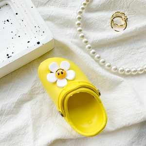 Detailed view of yellow clogs phone socket with smiley flower on white textured fabric