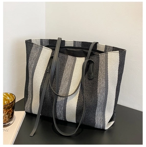 Vertical striped tote bag with leather straps displayed next to a glass and book