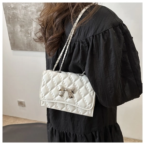 Detail of white quilted crossbody bag with silver bow accent and woven chain strap