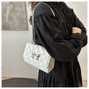 Detail of white quilted crossbody bag with silver bow accent and metal chain strap