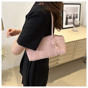 Sac sous le bras en cuir plissé rose avec logo doré porté par un mannequin en tailleur