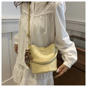 Detail of light yellow leather bucket bag with fashion embossing and colorful silk scarf