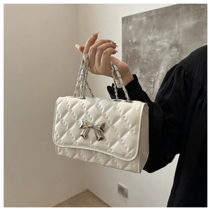 Detailed view of white quilted crossbody bag featuring silver metallic bow clasp