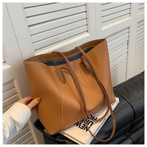 Detail of brown faux leather tote bag with white contrast stitching on a leather sofa