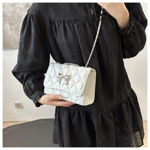 Detail of white quilted crossbody bag featuring a silver bow buckle and chain strap