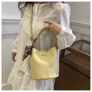 Detail of cream bucket bag with lychee texture leather, silk scarf handle, and fashion tag