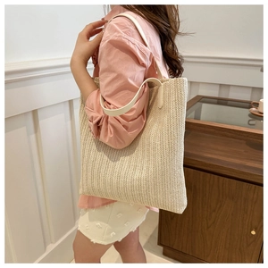 Close-up of beige woven tote bag with white leather straps worn over the shoulder