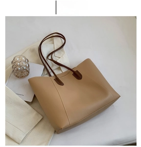 Detail of khaki tote bag with slim brown handles shown in a minimalist aesthetic setting