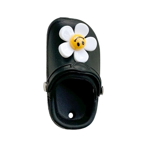 Miniature black clog phone grip with smiling white flower accessory on white background