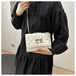 Close-up of white quilted leather bag featuring a silver bow buckle and metal chain strap
