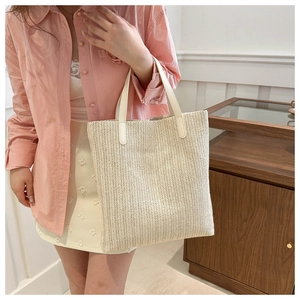 Detail of a beige woven straw tote bag with white faux leather handle worn by a model