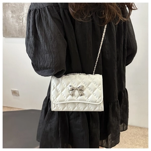 Detail of white quilted crossbody bag with silver bow clasp and metal chain strap