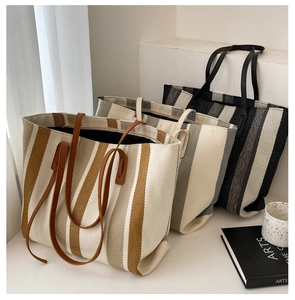 Close-up of canvas tote bags in brown, grey, and black vertical stripes with leather handles