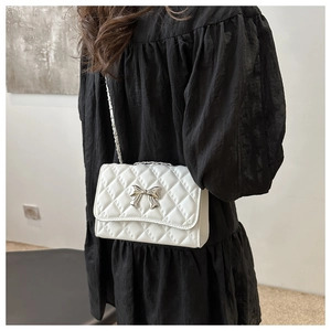 Detail of white quilted chain bag with silver bow accent worn on black dress