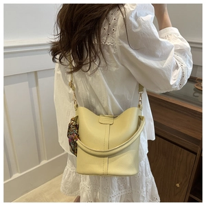 Detail of yellow bucket bag with lychee texture, silk scarf handle and chain strap