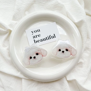 Close-up of cute white Maltese dog acrylic charms with blue bows on a white fabric background