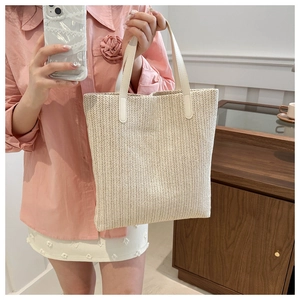 Close-up detail of the woven texture and white faux leather handle on the straw tote bag