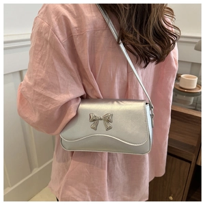 Detail showing the silver shoulder bag with a metallic bow and wavy edge flap design