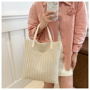 Close-up of beige woven tote bag with white leather straps and herringbone texture