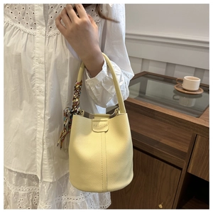 Detailaufnahme der blassgelben Eimer-Tasche aus Leder mit Seidenschal und FASHION-Prägung