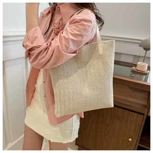Close-up of beige woven tote bag with herringbone texture and white leather handles