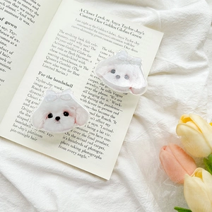 Close-up of two cute acrylic Maltese puppy phone grips with bows on a soft magazine background