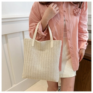 Detail of woven straw tote bag with cream leather straps on female model