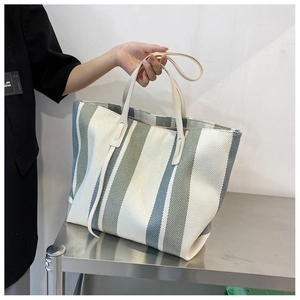 Detailed view of the large canvas tote with green vertical stripes and cream leather handles