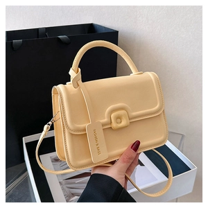 Detail of pale yellow crossbody handbag with top handle next to shopping packaging