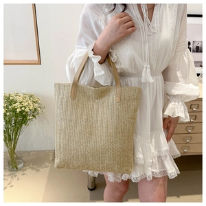Detail of hand-woven straw tote bag with brown leather handles and summer beach aesthetic