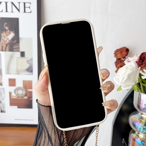 Detail of cream phone case with gold crossbody chain, hand-held near elegant flowers