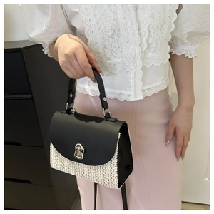 Detail of elegant woven straw handbag with black leather flap and metallic twist lock