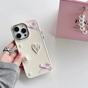 Detail of cream iPhone case with pink plaid bows, metallic heart, and elegant pearls