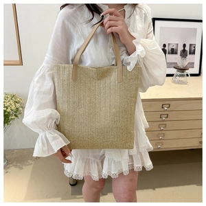 Detail of beige woven tote bag with brown leather handles in a home setting