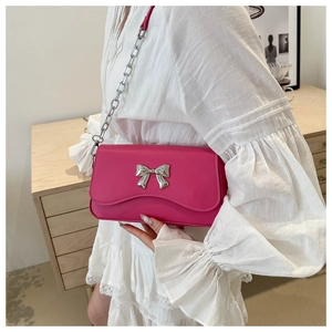 Detail of fuchsia leather shoulder bag with silver bow buckle and chain strap on a model