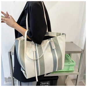Detailed close-up of a large striped tote bag with leather straps on a model's shoulder