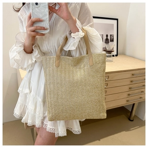 Macro detail of the woven herringbone texture and leather handle on the beige tote bag