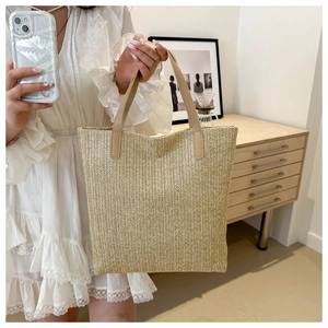 Detail view of woven straw tote bag with fine textures and white leather handles