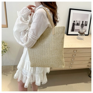 Detail of straw woven tote bag with slim leather straps worn over a white lace dress