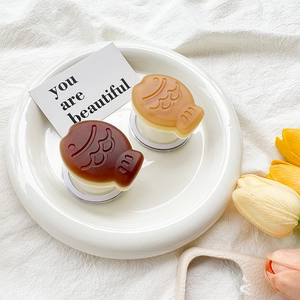 Macro detail of matte Taiyaki-shaped phone grips in brown and khaki on a white tray